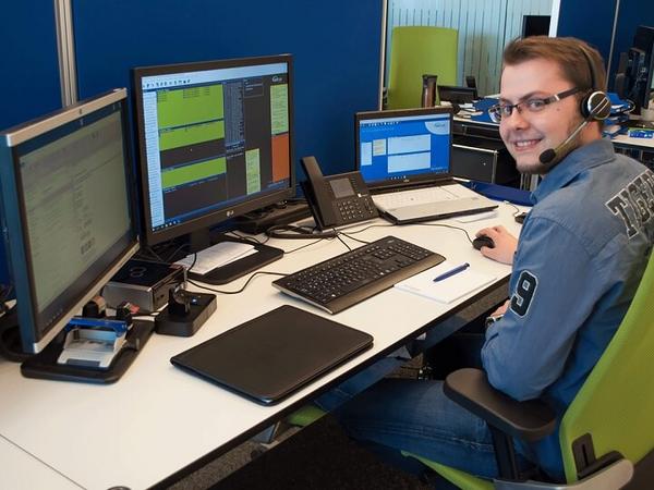 Ein Kollege arbeitet am Schreibtisch, spricht per Headset und organisiert Aufgaben an mehreren Monitoren.