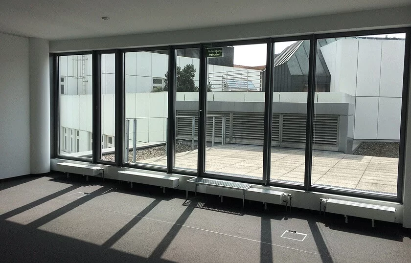 Jemand wischt den Boden eines großen, leeren Raums. Durch die hohen Fenster fällt Licht auf die weiße Terrasse draußen.