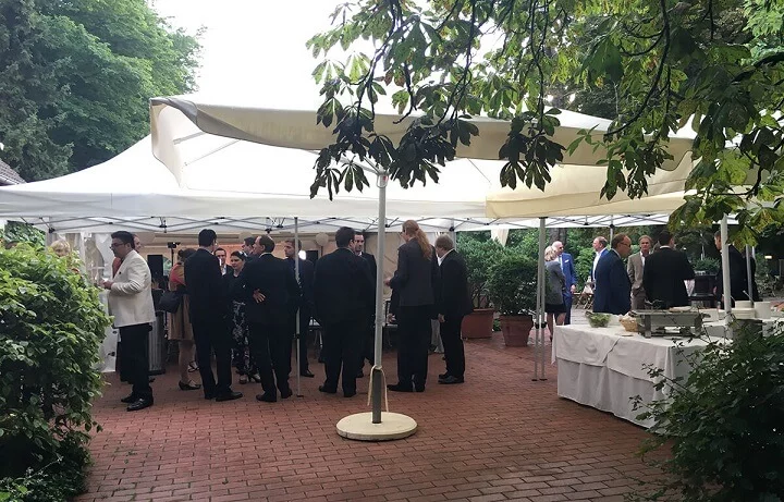 Mehrere Menschen richten draußen unter weißen Zelten ein Buffet an und besprechen gemeinsam den Ablauf des Events.